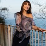 Segunda foto de modelo con la blusa de CHB Art&Design apoyada en la barandilla, con el estampado del interior de una casa y vistas a la Bahía de La Concha.